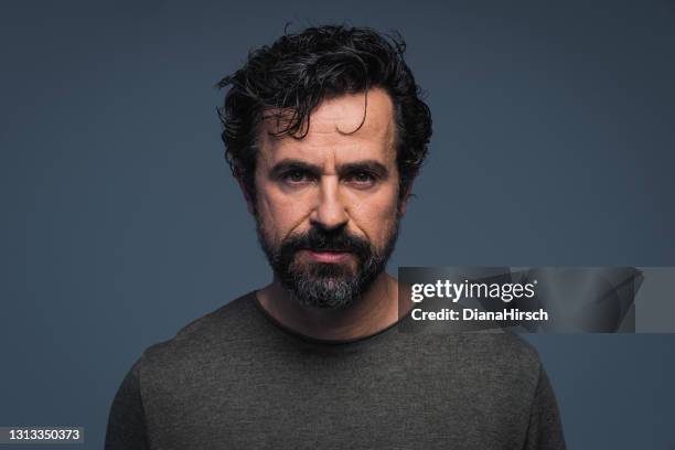 studio head shot of a handsome mature man with natural black and gray hair looking at camera on grey background - facial hair stock pictures, royalty-free photos & images