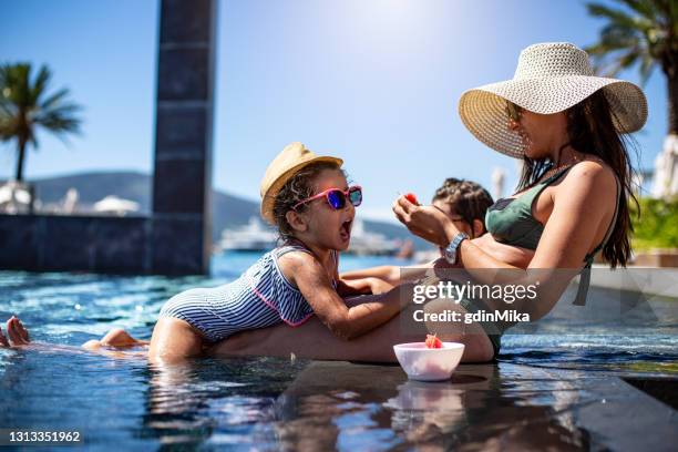 schöne aufgeregte frau mit kleinen schönen töchtern haben spaß im sommer schwimmbad, während sie im hotel ruhen, während wassermelone essen - eltern sonnenbrille sonne lachen stock-fotos und bilder