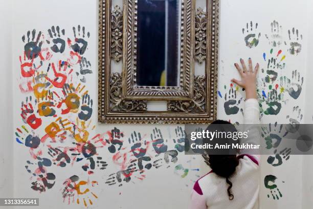 a young girl making multicolor hand print paintings on wall around a silver mirror. - paint handprint stock pictures, royalty-free photos & images
