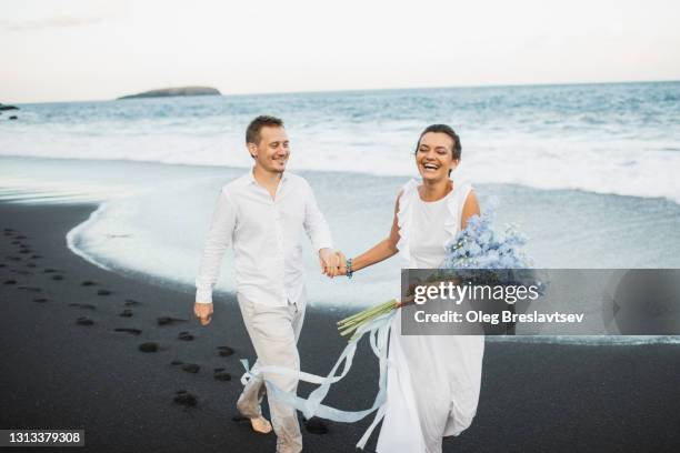 happy wedding couple running by the beach and laughing. romantic feelings and vibes. togetherness - beach vibes stock-fotos und bilder