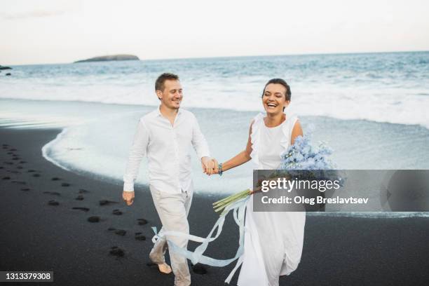 happy wedding couple running by the beach and laughing. romantic feelings and vibes. togetherness - married stockfoto's en -beelden