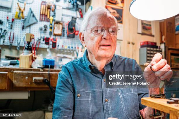 close-up shot of a senior caucasian man inspecting  a fishing fly in his man cave under a desk lamp indoors - finger hook stock pictures, royalty-free photos & images