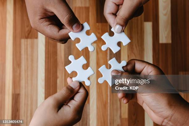 high angle view of human hands holding jigsaw pieces connection join together. partner unity teamwork and problems brainstorming concepts - 4 piece puzzle stockfoto's en -beelden