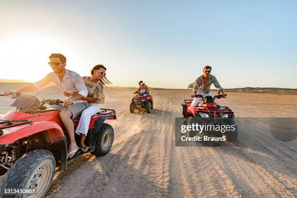 happy friends driving quads in the desert at sunset. - quadbike stock pictures, royalty-free photos & images