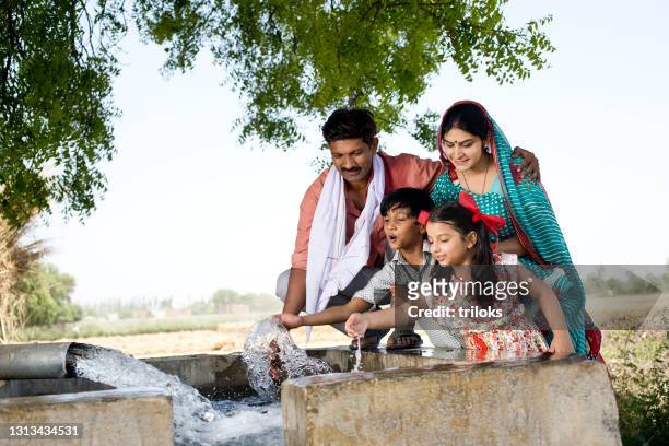 rural family having fun splashing water on field - rural indian family stock pictures, royalty-free photos & images