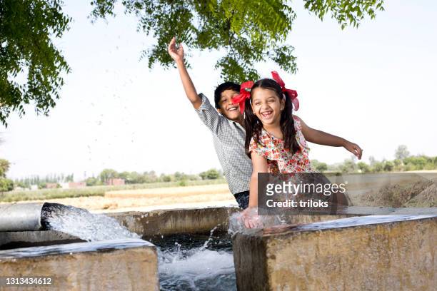 ragazzo e ragazza spruzzano acqua sul campo - village boy foto e immagini stock