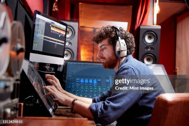 man working in music studio using computer wearing head phones - tv studio stock-fotos und bilder