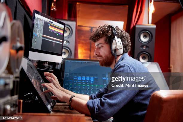 man working in music studio using computer wearing head phones - オーディオ ストックフォトと画像