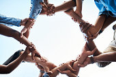 Low angle shot of an unrecognizable group of businesspeople standing together and holding each others arms in a circle