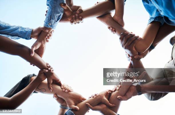 low angle shot of an unrecognizable group of businesspeople standing together and holding each others arms in a circle - community stock pictures, royalty-free photos & images