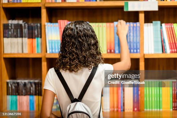 joven mirando libros en estanterías en una librería - libreria fotografías e imágenes de stock