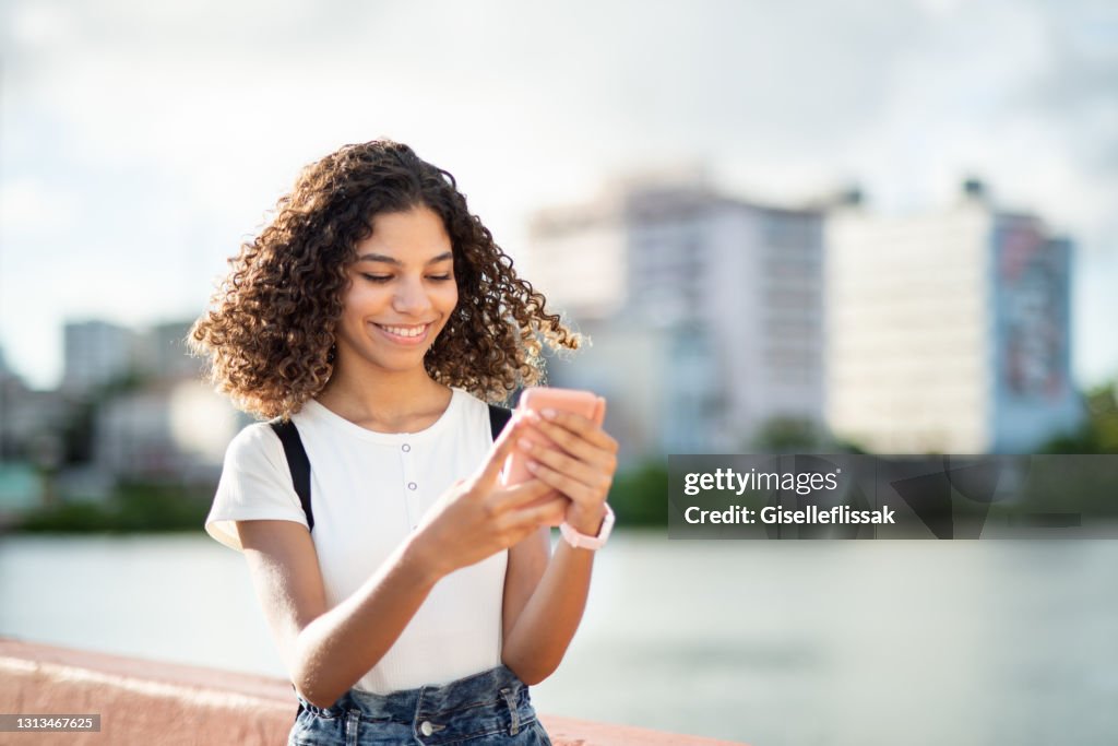 Lächelndes Mädchen, das draußen steht und einen Text auf ihrem Handy liest