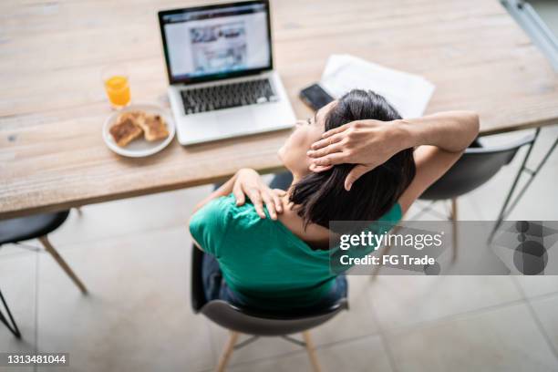 rear view of a woman stretching neck while working at home - neck stretch stock pictures, royalty-free photos & images