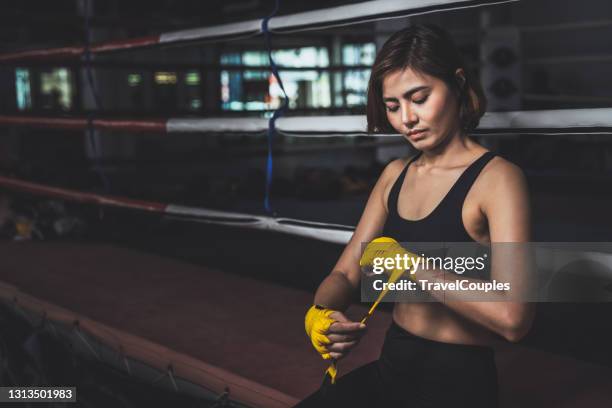 young female boxer wearing strap on wrist. woman in sports clothing preparing for boxing fight or workout. fitness young woman with muscular body preparing for boxing training at gym. - arte marziale foto e immagini stock