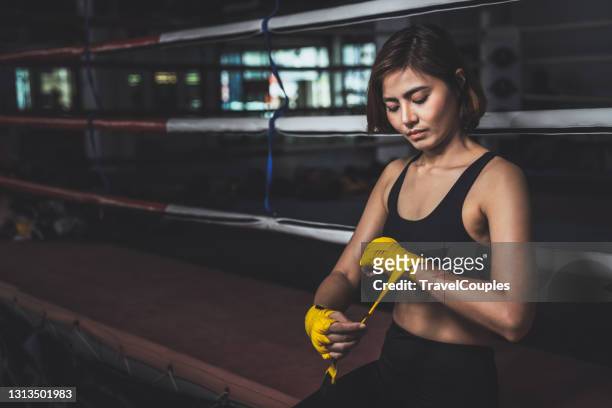 young female boxer wearing strap on wrist. woman in sports clothing preparing for boxing fight or workout. fitness young woman with muscular body preparing for boxing training at gym. - martial arts stock pictures, royalty-free photos & images