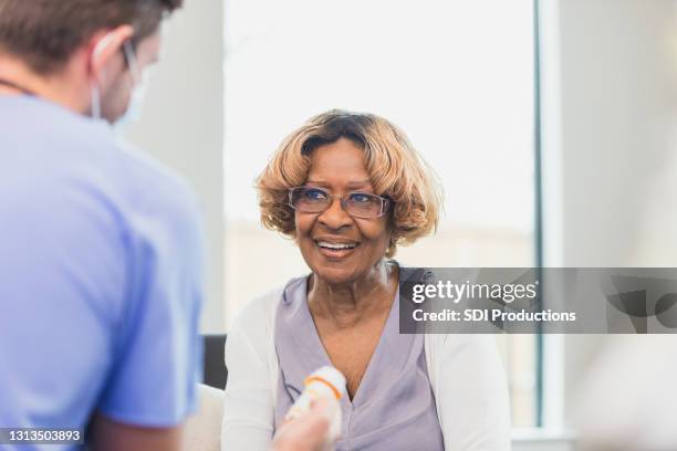 seniorin lächelt, als unkenntliche männliche krankenschwester erklärt medizin dosierung - nurse with old male patient home care stock-fotos und bilder