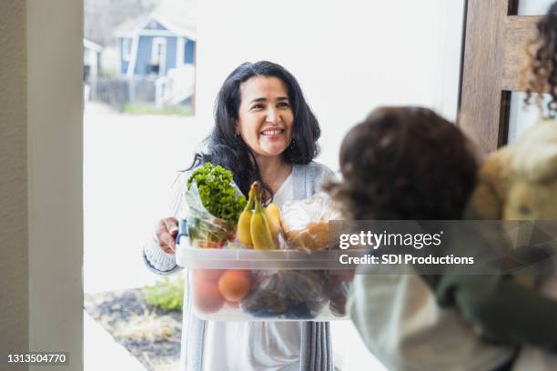 friendly neighbor brings food to unrecognizable mother and child - family smiling at front door stock pictures, royalty-free photos & images