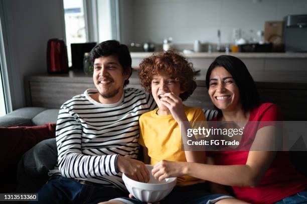 familie schaut fernsehen und essen popcorn zu hause - familie zuhause essen stock-fotos und bilder