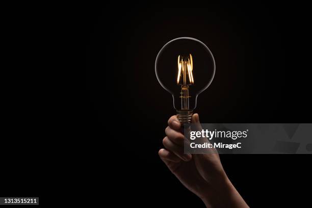 hand holding illuminated light bulb in the dark - bombillas fotografías e imágenes de stock