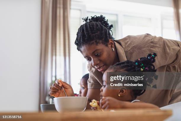 glückliches junges mädchen essen getreide mit milch zum frühstück in einer küche - black mother and child cooking stock-fotos und bilder