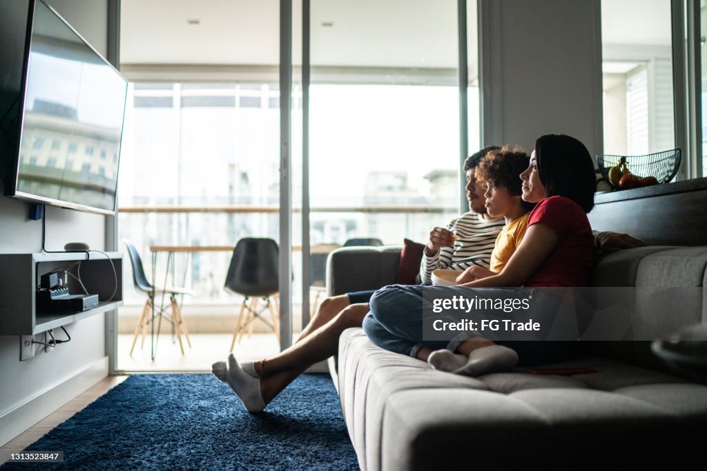 Famille regardant la tv et mangeant le maïs éclaté à la maison
