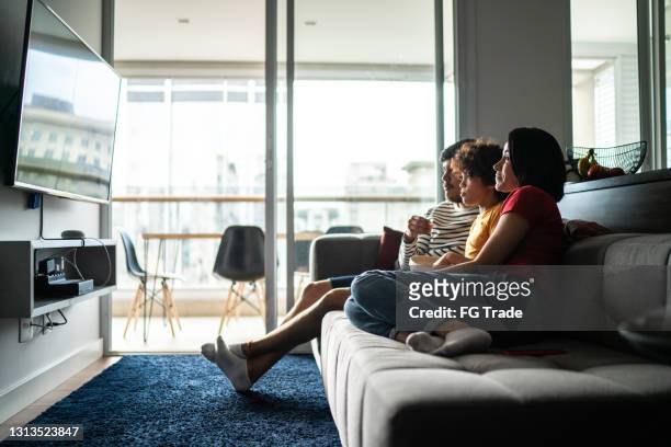 family watching tv and eating popcorn at home - watching stock pictures, royalty-free photos & images