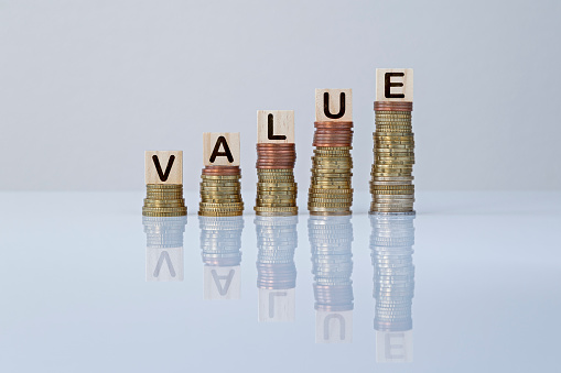 Word "VALUE" on wooden blocks on top of ascending stacks of coins against gray background.