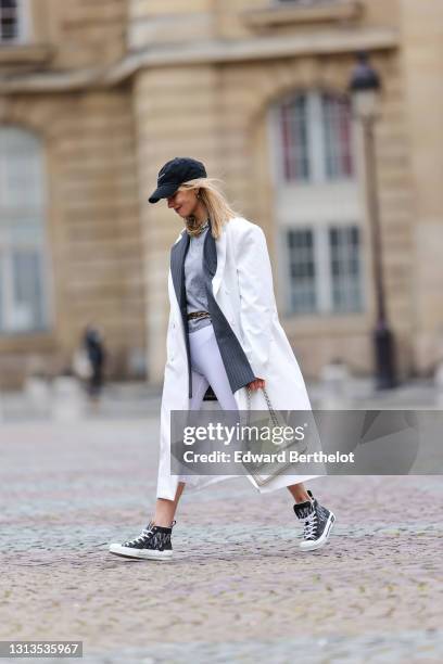 Natalia Verza @mascarada.paris wears a Nike cap hat, a gray striped oversized blazer jacket, a metallic chain necklace, a gray t-shirt, a white long...