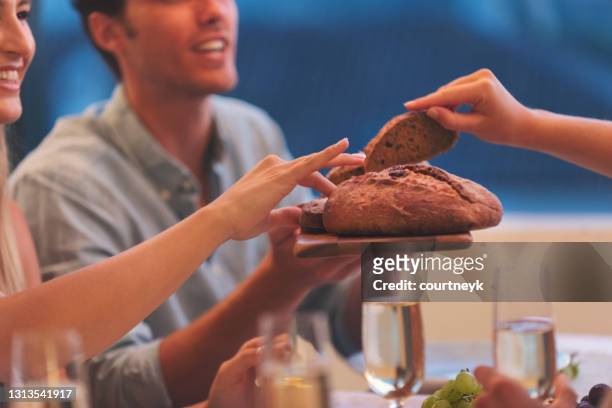 group of friends sharing a loaf of bread at a dinner party. - man offering bread stock pictures, royalty-free photos & images