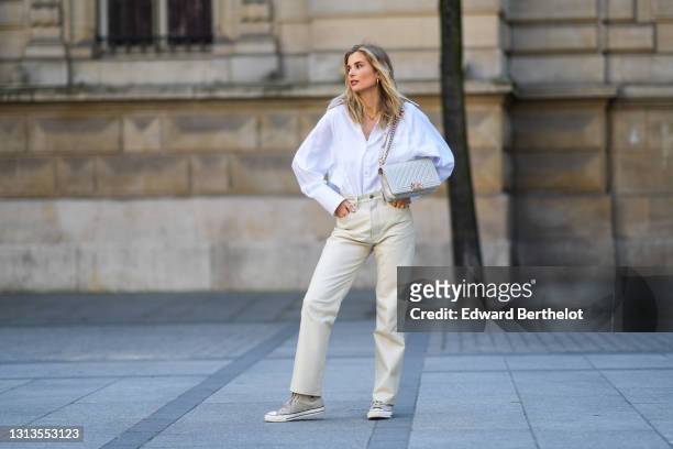 Xenia Adonts wears a white shirt with long collar from Attire The Studio, beige leather pants from Agolde, a white Chanel bag, Converse gray sneakers...