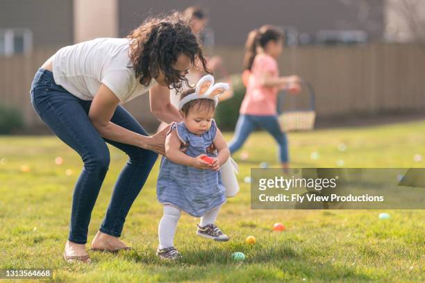 liebende mutter hilft entzückende kleinkind tochter mit ostereiersuche im freien - easter egg hunt stock-fotos und bilder