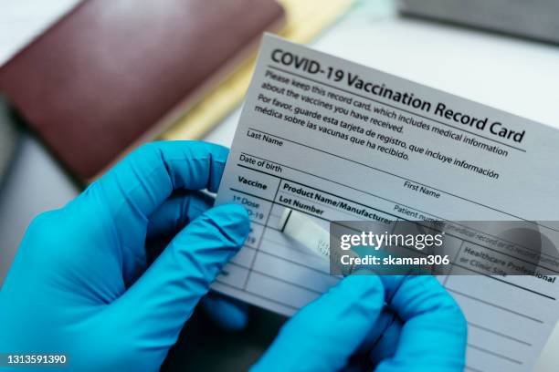 close up hand of doctor put label covid-19 vaccine sticker on vaccination certificate card and passport - immunisation certificate stock-fotos und bilder