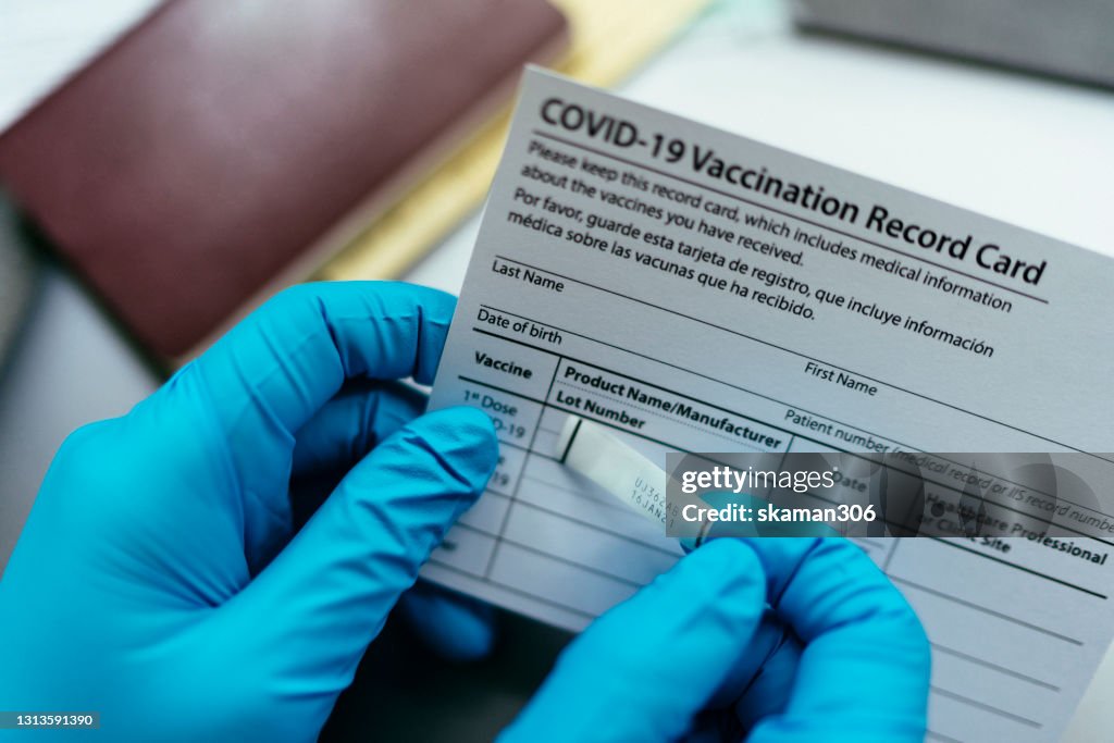 Close up hand of doctor put label covid-19 vaccine sticker on vaccination certificate card and passport