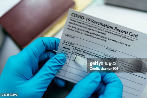 close up hand of doctor put label covid-19 vaccine sticker on vaccination certificate card and passport - immunization certificate stock pictures, royalty-free photos & images