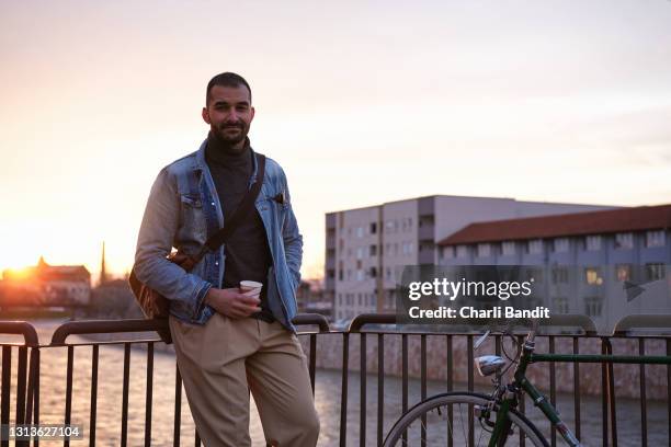 modische männliche touristen bewundern den sonnenuntergang blick von der brücke mit einer tasse kaffee, während seiner stadt erkundung - charmant stock-fotos und bilder