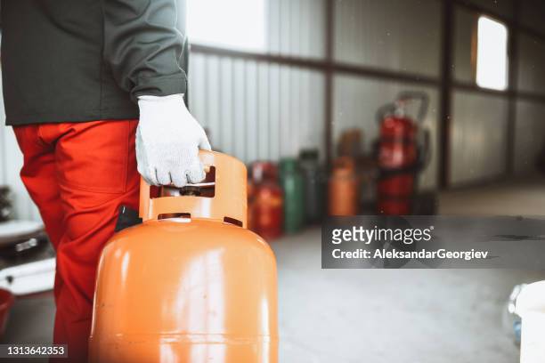 male worker carrying gas cylinder to storage room in liquefied gas store - gasoline storage stock pictures, royalty-free photos & images