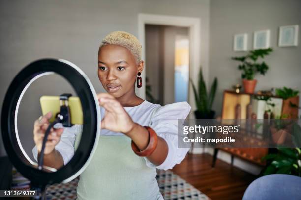 jovem influenciadora africana ajustando seu telefone inteligente antes de um vlog post - youtube - fotografias e filmes do acervo