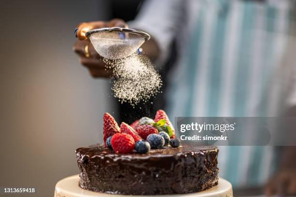 woman's hand dusting caster sugar on chocolate cake - icing sugar stock pictures, royalty-free photos & images