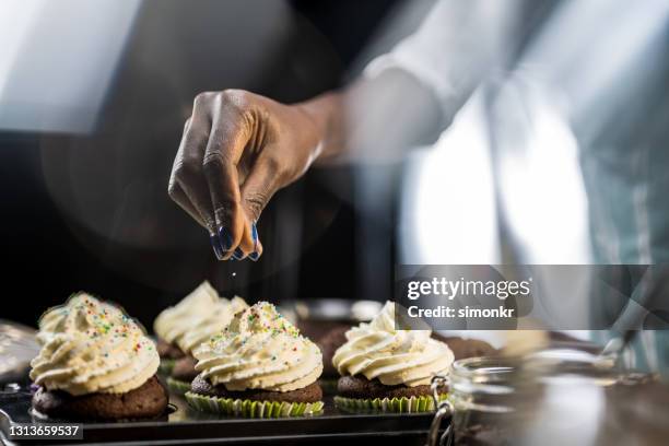 de hand die van de vrouw honderden en duizenden op cupcake besprenkelt - black room stockfoto's en -beelden