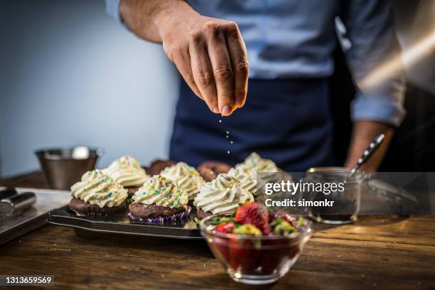 de hand die van de mens honderden en duizenden op cupcake besprenkelt - strooisels stockfoto's en -beelden