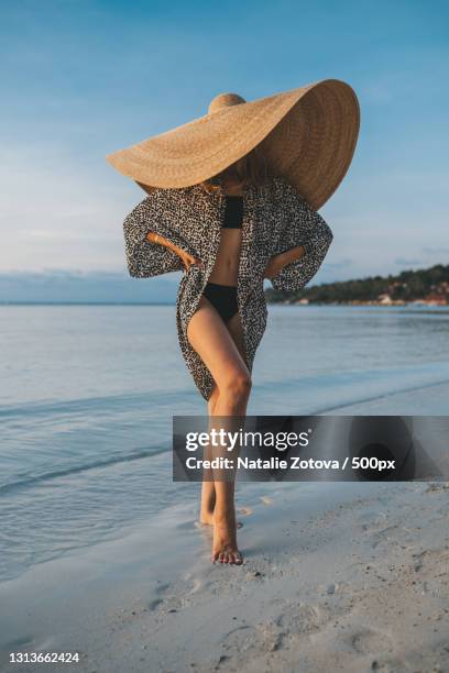 portrait of a blonde woman with an oversized straw hat on the beach - fashion millinery woman stock-fotos und bilder