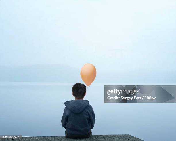 rear view of person sitting at waters edge holding a balloon - pureté photos et images de collection