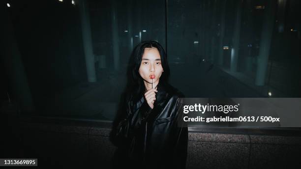 young woman with a lollipop in a leather jacket outside at night in the city - night in fotografías e imágenes de stock