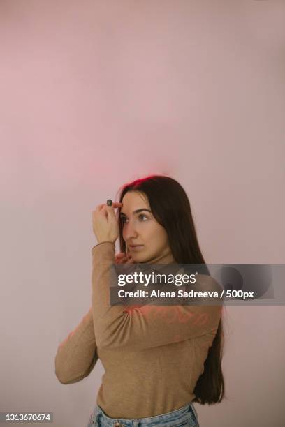 young woman looking away while standing against pale pink wall,russia - gel effect stock pictures, royalty-free photos & images