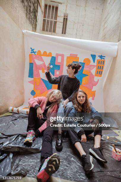 portrait of stylish young women sitting together against painting backdrop,avignon,france - photo shoot stock pictures, royalty-free photos & images