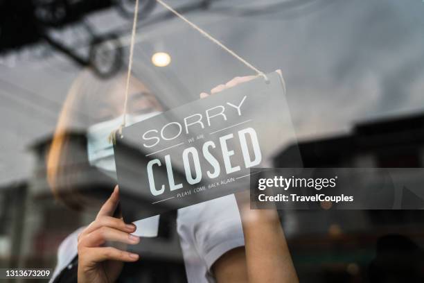 young asian woman wearing face mask and hand turning closed sign board on glass door in coffee shop and restaurant after coronavirus lockdown quarantine. business crisis concept. - closed stock pictures, royalty-free photos & images