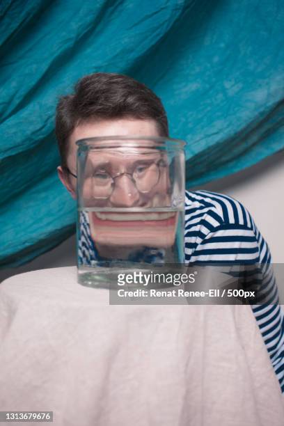 young man with eyeglasses in studio with glass beaker and teal drapes - verdraaid stockfoto's en -beelden