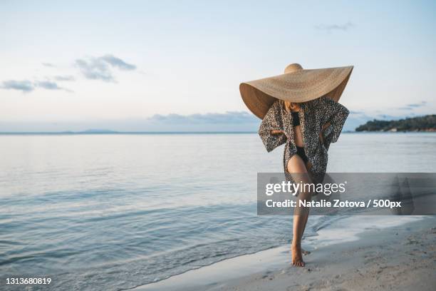 portrait of a blonde woman with an oversized straw hat on the beach - sonnenhut stock-fotos und bilder