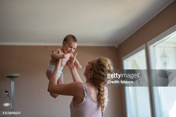 smiling mother holding baby boy in the living room. - adult diaper stock pictures, royalty-free photos & images