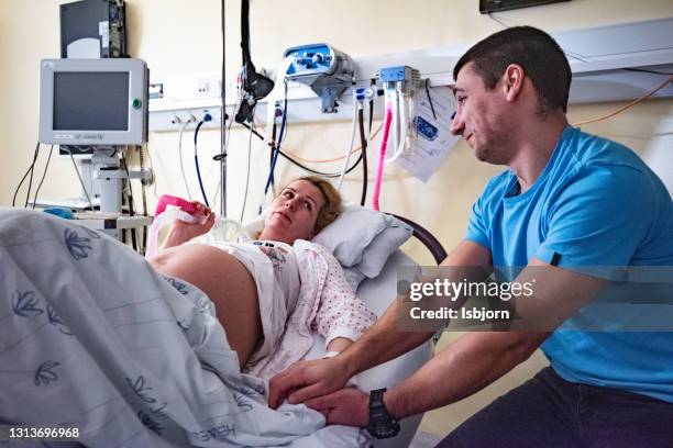 woman in labor in delivery room, holding husband's hand. - delivery room stock pictures, royalty-free photos & images